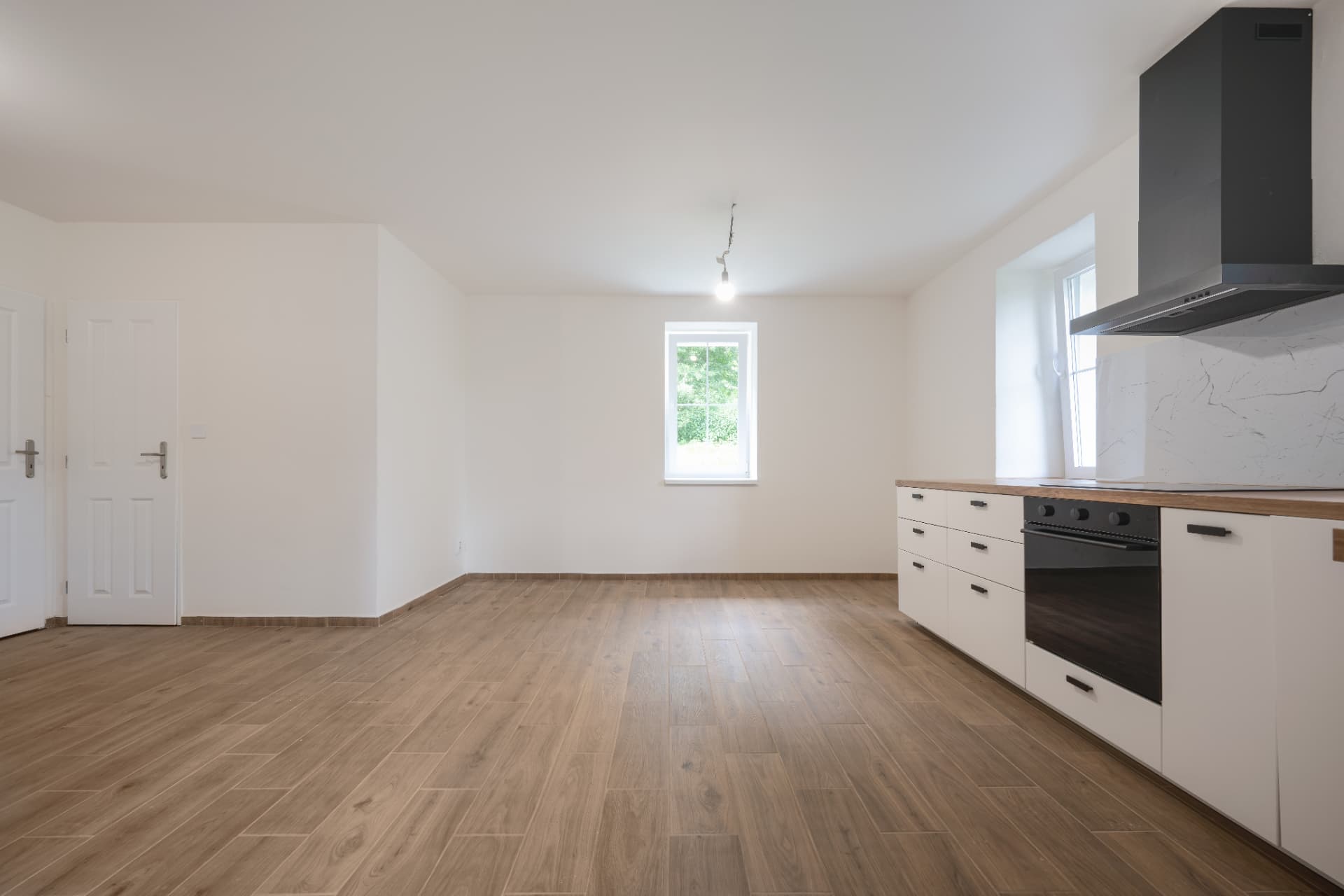 Pohled do obývacího pokoje s kuchyňskou linkou a oknem do zeleně